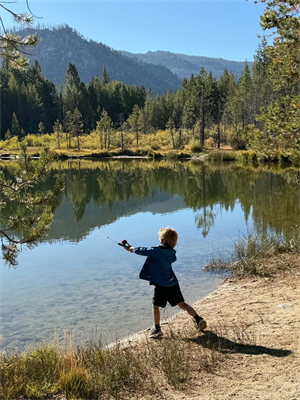 Picture of a young boy casting a fishing line into the lake while facing away from the camera.