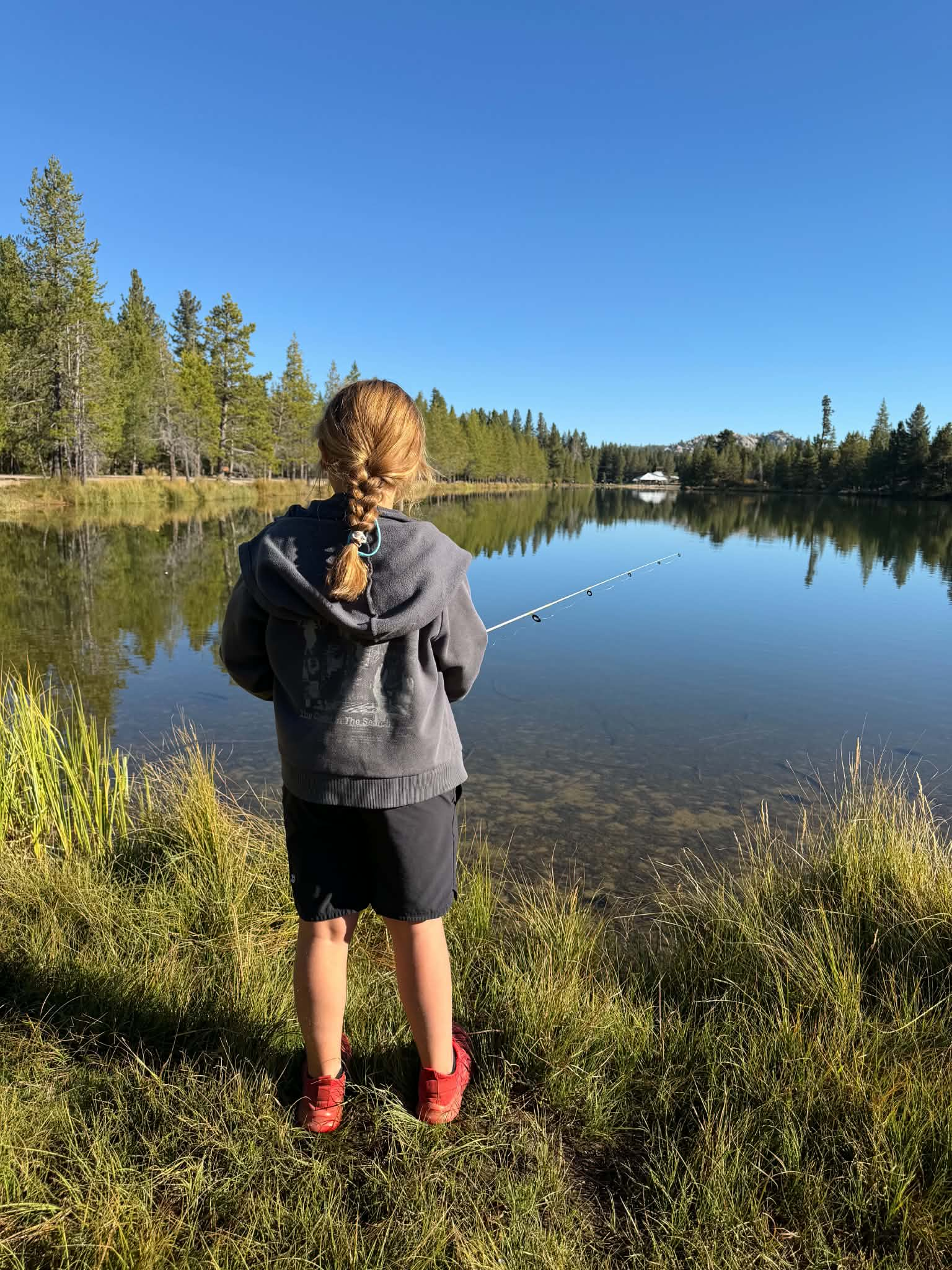 Picture of a young girl fishing at a lake and facing away from the camera
